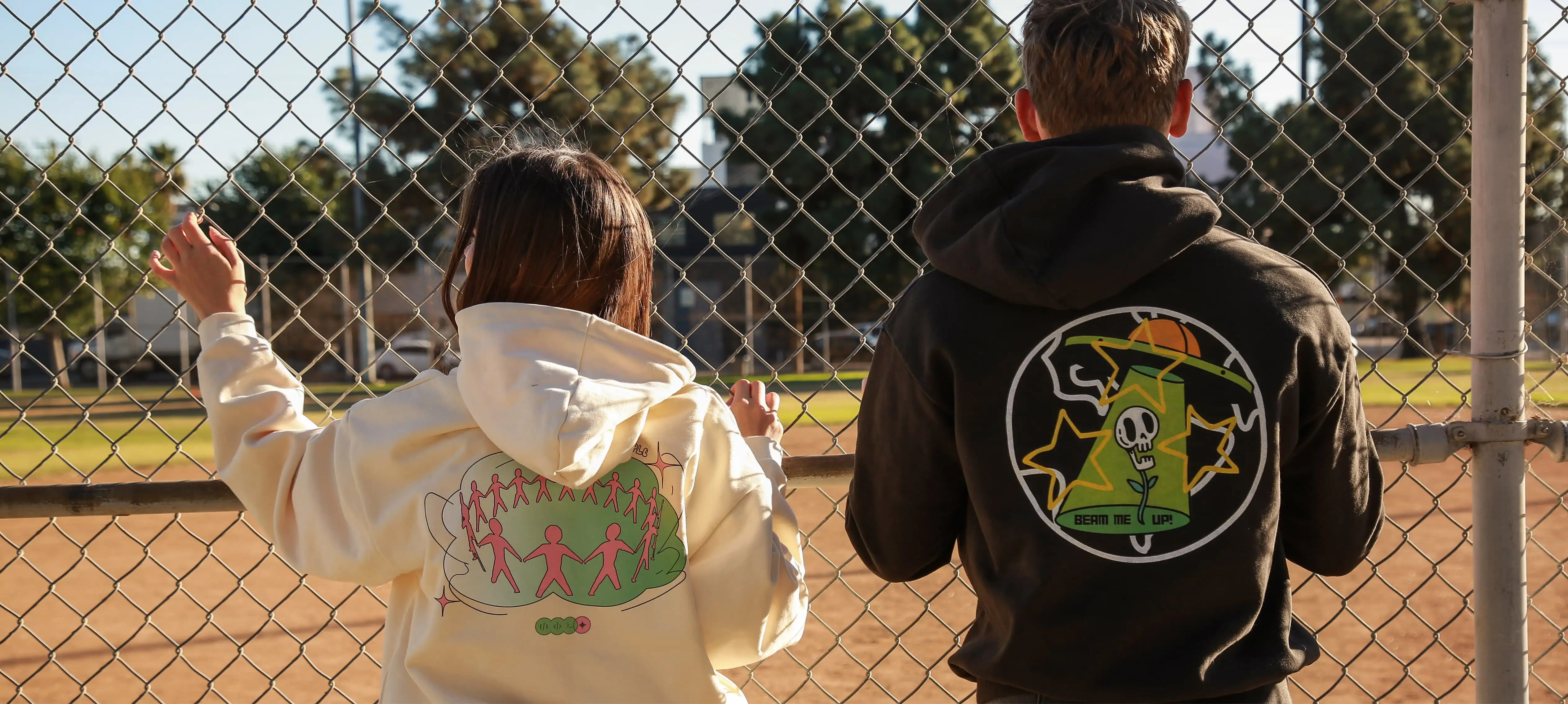 A man and a woman, wearing custom Tapstitch hoodies, are standing near the iron fence.