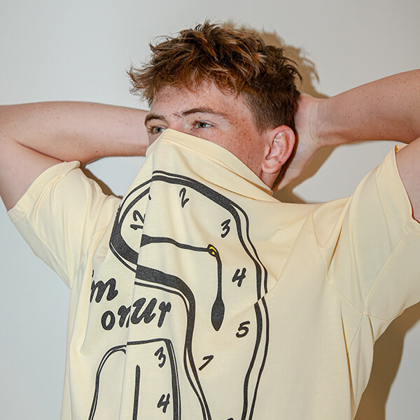 Male model wearing oversized graphic t-shirt with abstract face design covering mouth
